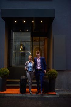 Young business people couple entering city  hotel, looking for room, holding suitcases while walking on street