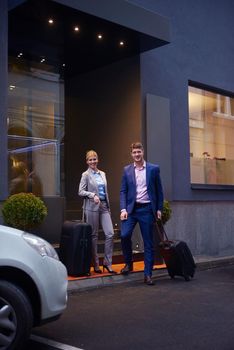 Young business people couple entering city  hotel, looking for room, holding suitcases while walking on street