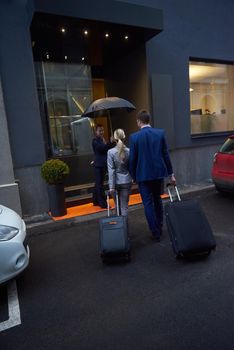 Young business people couple entering city  hotel, looking for room, holding suitcases while walking on street