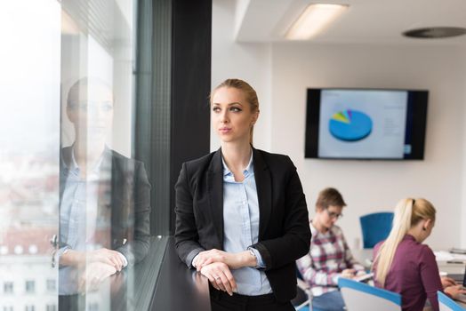 portrait of young business woman at modern startup office interior, team in meeting group in background