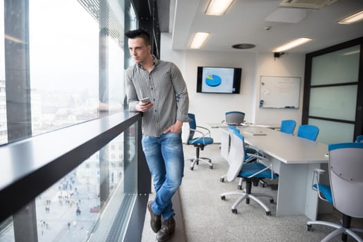 relaxed young businessman using smart phone at modern startup business office meeting room  with big window and city in backgronud