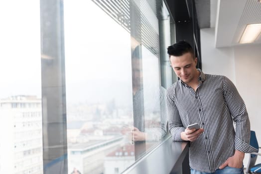 relaxed young businessman using smart phone at modern startup business office meeting room  with big window and city in backgronud