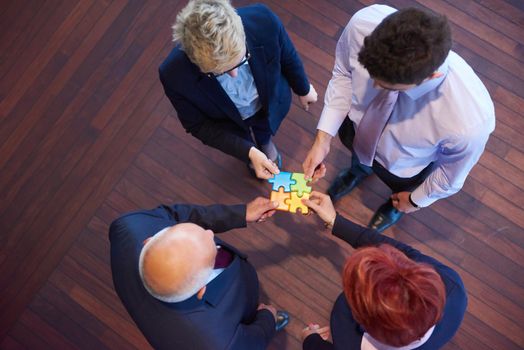 business people group assembling jigsaw puzzle and represent team support and help concept, top view perspective at modern bright office interior