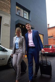 Young business people couple entering city  hotel, looking for room, holding suitcases while walking on street