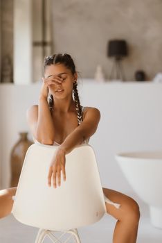 Girl in lingerie sits on a chair with closed eyes. Poses at the camera.