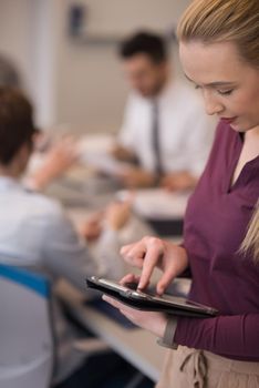 Blonde businesswoman in casual  clothes working on tablet computer at modern startup business office interior. Young people group on team meeting blured  in background