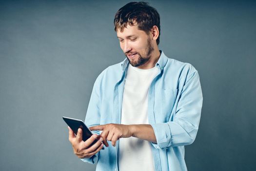 A middle-aged white Caucasian man holds a tablet in his hand and looks at a mobile application. A satisfied guy uses the Internet from a mobile device.