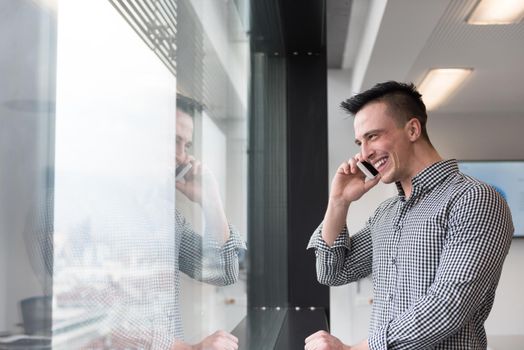 relaxed young businessman speaking on smart phone at modern startup business office meeting room  with big window and city in backgronud