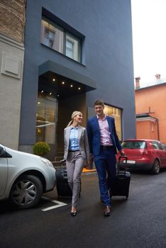 Young business people couple entering city  hotel, looking for room, holding suitcases while walking on street