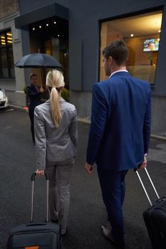 Young business people couple entering city  hotel, looking for room, holding suitcases while walking on street