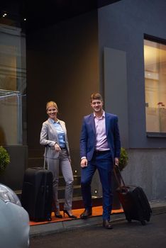 Young business people couple entering city  hotel, looking for room, holding suitcases while walking on street