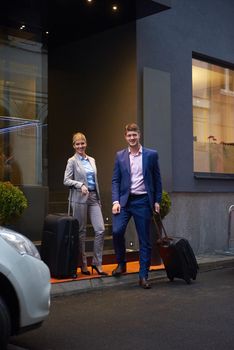 Young business people couple entering city  hotel, looking for room, holding suitcases while walking on street