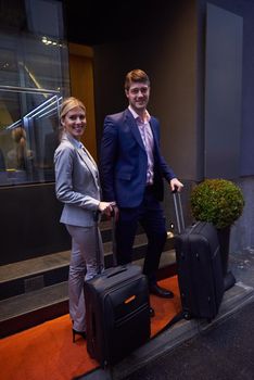 Young business people couple entering city  hotel, looking for room, holding suitcases while walking on street