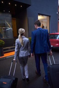 Young business people couple entering city  hotel, looking for room, holding suitcases while walking on street