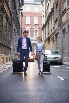 Young business people couple entering city  hotel, looking for room, holding suitcases while walking on street