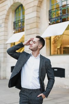 Young cacuasian male person wearing suit standing near building outdoors. Concept of fashion and businessman, urban life.