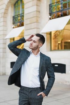 Young cacuasian male person wearing suit standing near building outdoors. Concept of fashion and businessman, urban life.