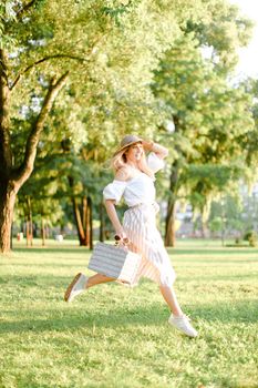 Young happy woman jumping in park and running, wearing fashionable clothes and hat. Concept of summer sales and style.