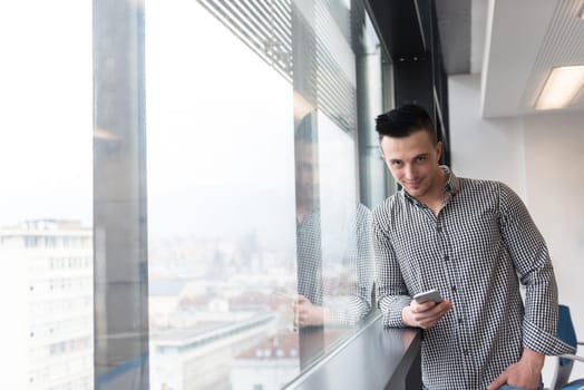 relaxed young businessman using smart phone at modern startup business office meeting room  with big window and city in backgronud