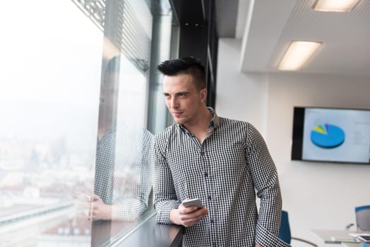 relaxed young businessman using smart phone at modern startup business office meeting room  with big window and city in backgronud