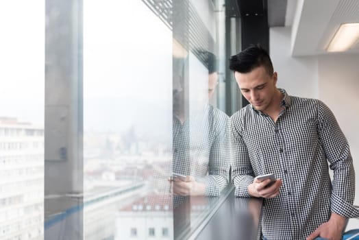 relaxed young businessman using smart phone at modern startup business office meeting room  with big window and city in backgronud