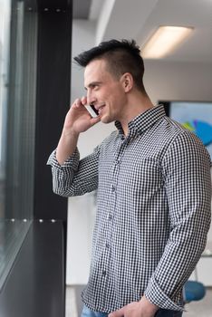 relaxed young businessman speaking on smart phone at modern startup business office meeting room  with big window and city in backgronud