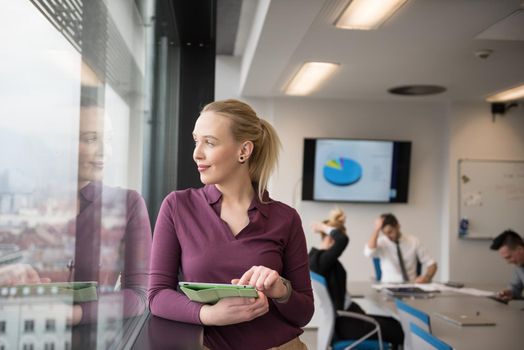 Blonde businesswoman in casual  clothes working on tablet computer at modern startup business office interior. Young people group on team meeting blured  in background