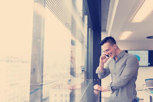 relaxed young businessman speaking on smart phone at modern startup business office meeting room  with big window and city in backgronud