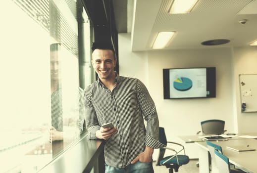 relaxed young businessman using smart phone at modern startup business office meeting room  with big window and city in backgronud