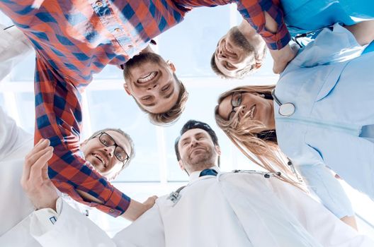 A large diverse medical team standing in a circle, everyone is looking down at the camera and smiling, isolated on white with a central copyspace