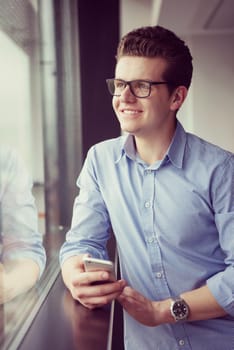 businessman using a phone beside window of modern office