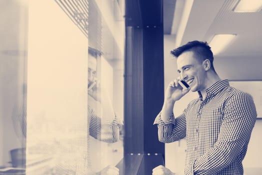 relaxed young businessman using smart phone at modern startup business office meeting room  with big window and city in backgronud