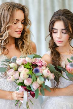 Two young caucasian brides with bouquets at studio. Concept of bridal photo session, wedding and floristic art.