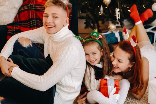 a happy family is lying on the floor of the house with New Year's gifts, next to the Christmas tree,