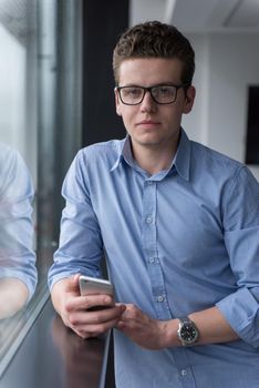 businessman using a phone beside window of modern office