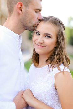 Happy groom kissing bride and holding hands outdoors. Concept of wedding and bridal photo session, relationship.