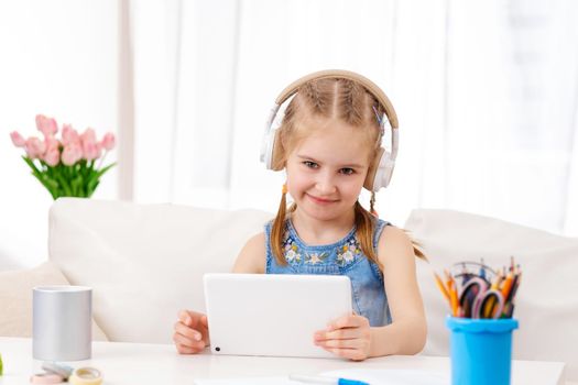 Beatiful little girl with white tablet with headphones on, in the room