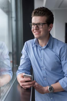 businessman using a phone beside window of modern office