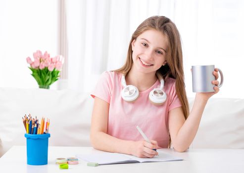 Hardworking teen is preparing for exams with music and cup of water in hand