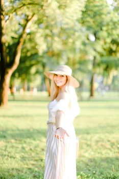 Young cute girl wearing hat and standing in garden, focus on hand. Concept of beautiful female person, summer fashion and walking in park.