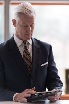 handsome senior business man with grey hair working on tablet computer at modern bright office interior