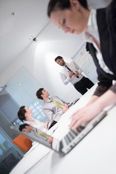 young business woman on meeting usineg laptop computer, blured group of people in background at  modern bright startup office interior taking notes on white flip board and brainstorming about plans and ideas