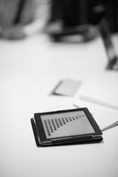 Close up of tablet touchpad computer with focus on business analytics and progress chart document. Business people group on meeting in background