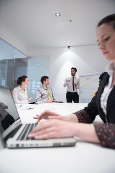 young business woman on meeting usineg laptop computer, blured group of people in background at  modern bright startup office interior taking notes on white flip board and brainstorming about plans and ideas