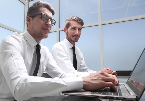 young colleagues sit at the desk in the office and work on laptops