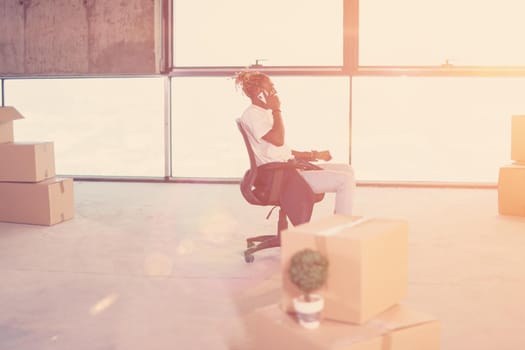 young casual african american businessman using a mobile phone while taking a break on construction site with sunlight through the windows during moving in at new startup office