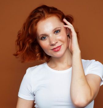 young pretty redhead girl posing cheerful on warm brown background, lifestyle people concept close up