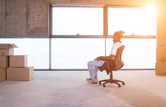 young casual african american businessman using a mobile phone while taking a break on construction site with sunlight through the windows during moving in at new startup office