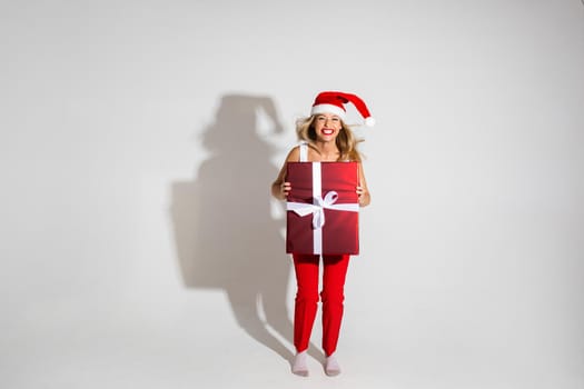 handsome woman with red and white christmas hat holds a big box with gift and jumps