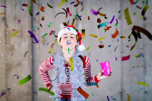 young happy casual business woman wearing a red hat and blowing party whistle while having new years confetti party in front of concrete wall